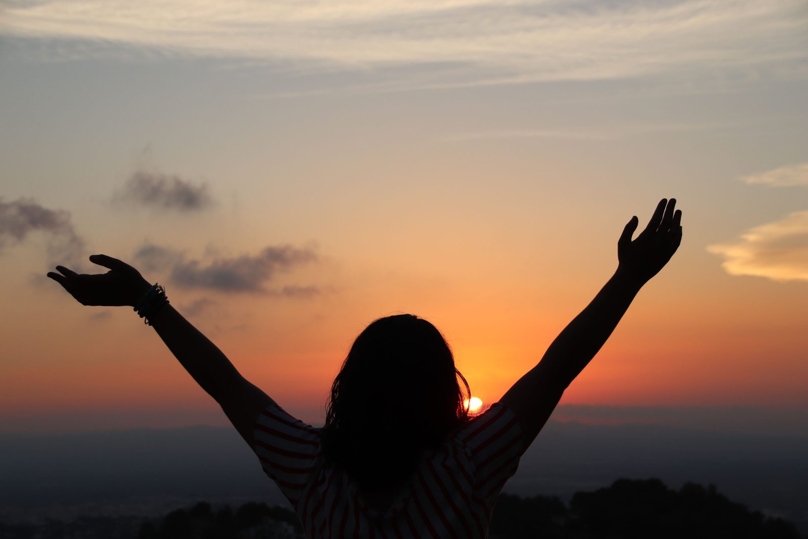 Una mujer abriendo sus brazos mientras ve el atardecer