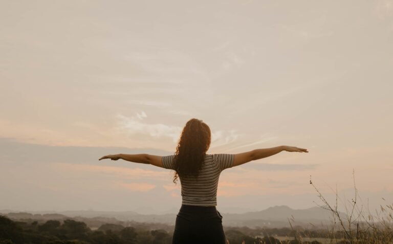 Mujer contemplando el horizonte, de espaldas, con los brazos abiertos.